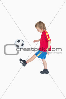 Side view of little boy kicking football