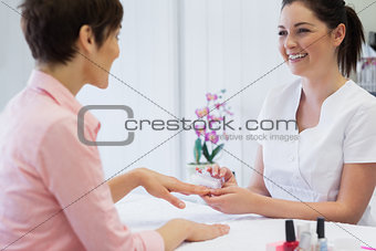 Happy young manicurist using nail brush on womans nails
