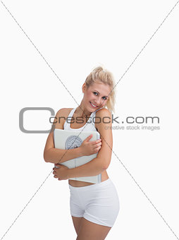 Portrait of young happy woman hugging weighing scales