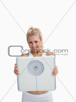 Portrait of young happy woman holding out weighing scales