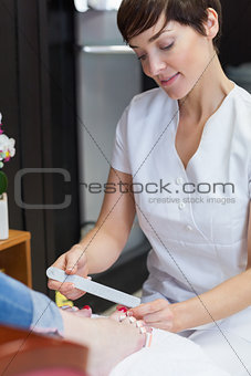 Nail technician filing womans toe nails at nail salon