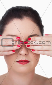 Sensuous young woman covering eyes with red painted finger nails