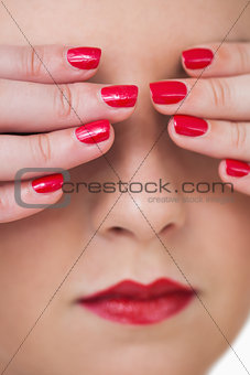 Macro shot of young woman covering eyes with red painted finger nails