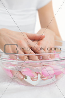 Womans hands in bowl with petals at hands spa