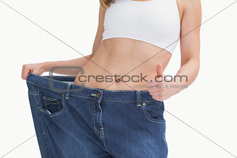 Midsection of woman wearing old pants after losing weight and gesturing thumbs up