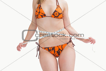 Midsection of young woman in bikini measuring waist