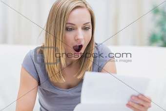 Shocked woman reading letter in living room