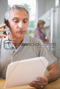 Focused mature man calling with a sheet of paper