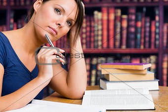 Woman thinking with pen and book in library