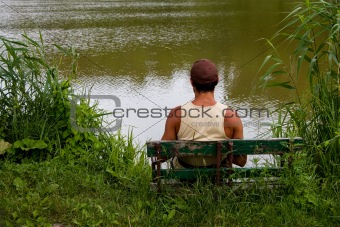 man is sitting on bench on lake