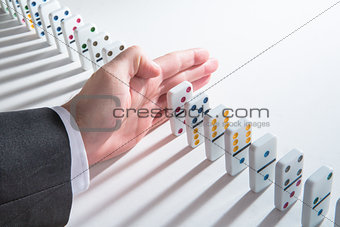 Hand resting in the middle of a line of dominoes about to push