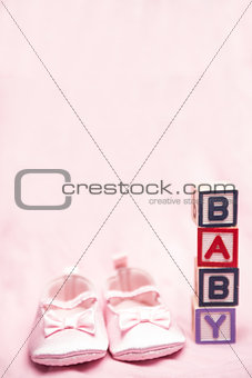 Baby girls pink booties beside blocks spelling baby