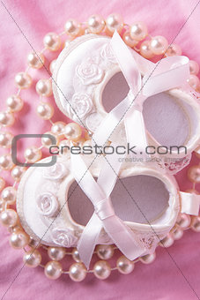 Overhead of white baby booties with string of pearls