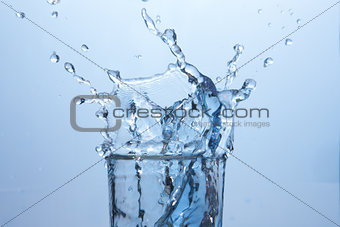 Close up on ice cube falling into glass of water