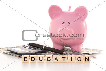 Piggy bank beside calculator and education spelled out in plastic letter pieces
