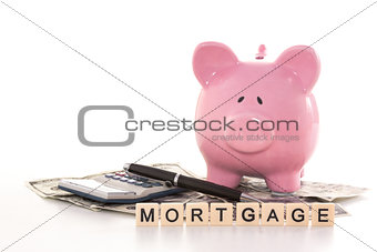 Piggy bank beside calculator and mortgage spelled out in plastic letter pieces