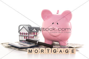 Piggy bank beside calculator miniature house and mortgage spelled out in plastic letter pieces