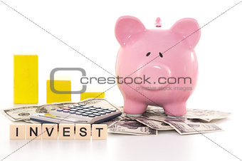 Piggy bank beside graph calculator and invest spelled out in plastic letter pieces
