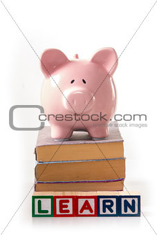 Piggy bank standing on stack of books with learn spelled out in blocks