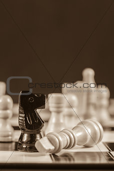 Fallen white chess piece lying next to black knight in sepia tone