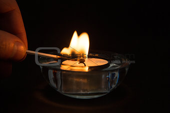 Hand lighting tea light candle in the dark