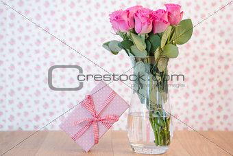Bouquet of pink roses in vase with pink gift leaning against it