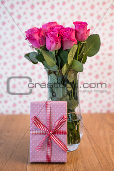 Bunch of pink roses in vase with pink gift leaning against it