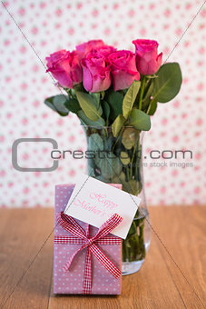 Bunch of pink roses in vase with pink gift leaning against it and mothers day card
