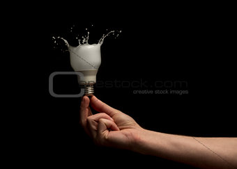 Hand holding light bulb turning to paint