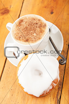 Fresh donut and cup of cappuccino on wooden table