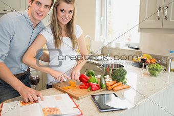 Woman cutting vegetables with man reading the cookery book