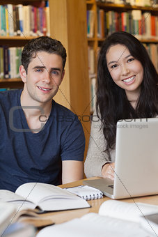 Two students learning with a laptop in a library