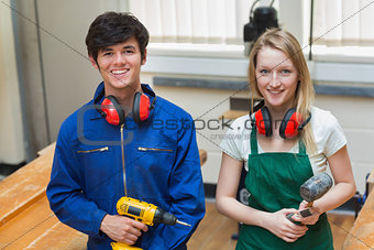 Two students holding a driller and a hammer