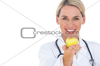 Happy doctor holding out apple and looking at camera