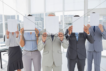 Buisness team holding up blank pages and covering their faces