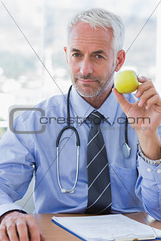 Doctor sitting behind his desk holding a green apple