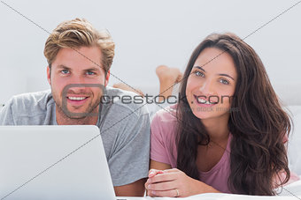 Cheerful couple using laptop in bed