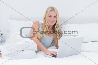 Woman using her laptop laid on her bed