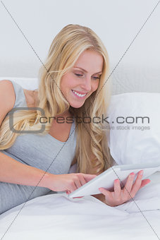 Cheerful woman touching her tablet in bed