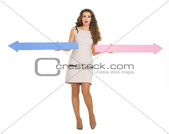 Full length portrait of confused young woman pointing in opposit