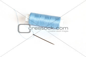 Blue bobbin of thread with needle on white