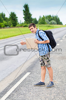 Boy hitchhiker on the road waiting for car to stop in summer
