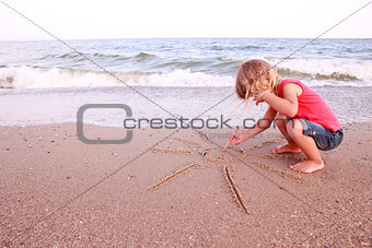  girl draws a sun in the sand on the beach
