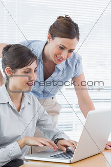Businesswoman leaning over to look at colleagues laptop