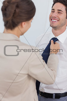 Woman helping her smiling husband to tie his tie
