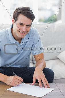 Portrait of a man writing on a paper while he is sat on a couch