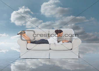 Businesswoman lying on couch and typing on her laptop