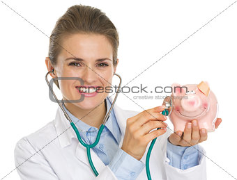 Smiling doctor woman listening piggy bank with stethoscope