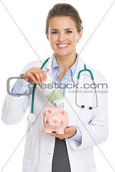 Smiling doctor woman putting euros banknote in piggy bank