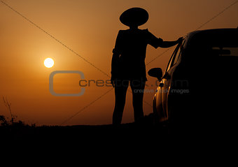 Silhouette woman with hat standing near car